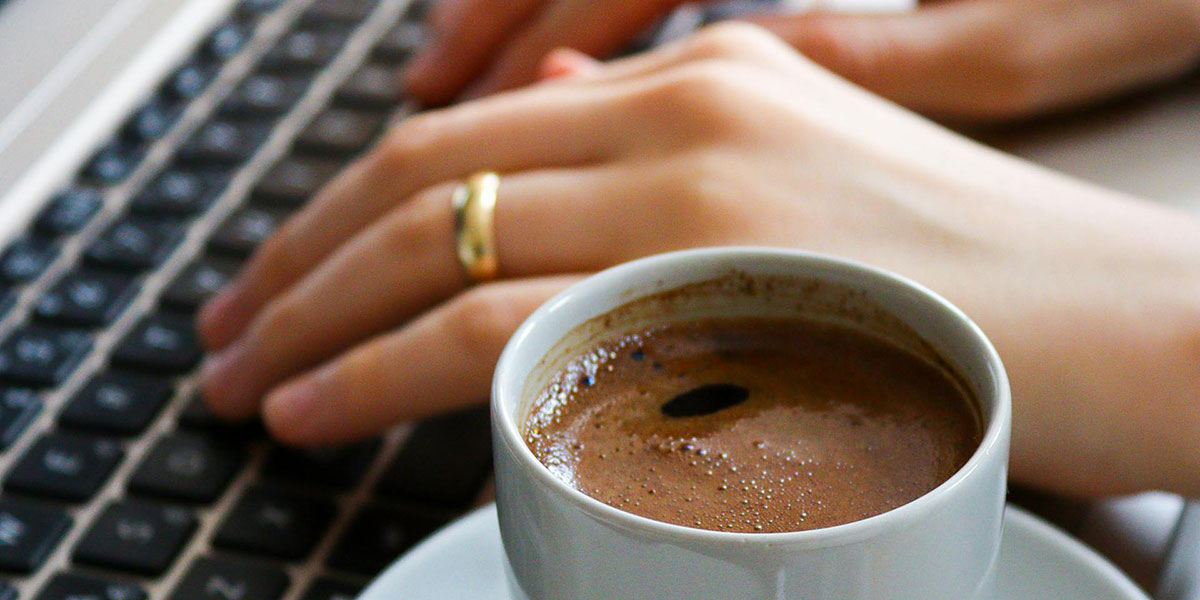 Close up of a person typing on a keyboard with a cup of coffee